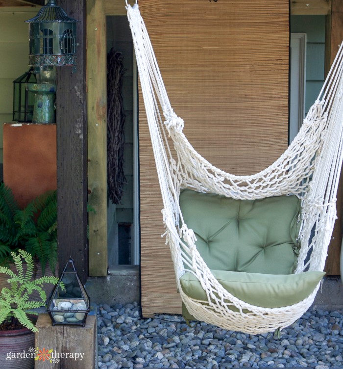 Silla colgante de macramé blanco con cojín verde en un patio trasero