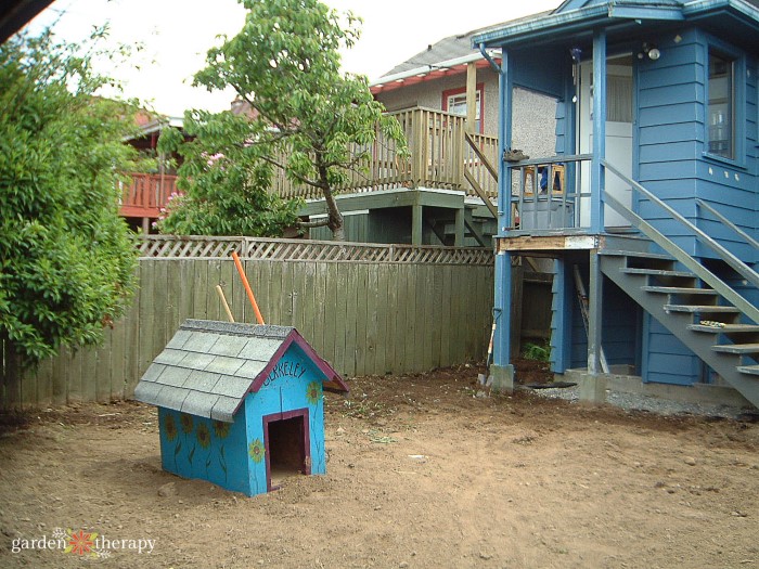 Fenced in backyard covered in dirt with a blue doghouse.