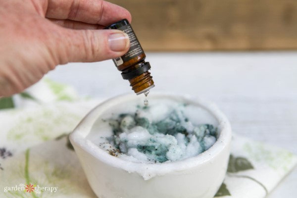 Mujer añadiendo gotas de aceite esencial en un bol de exfoliante de azúcar casero.