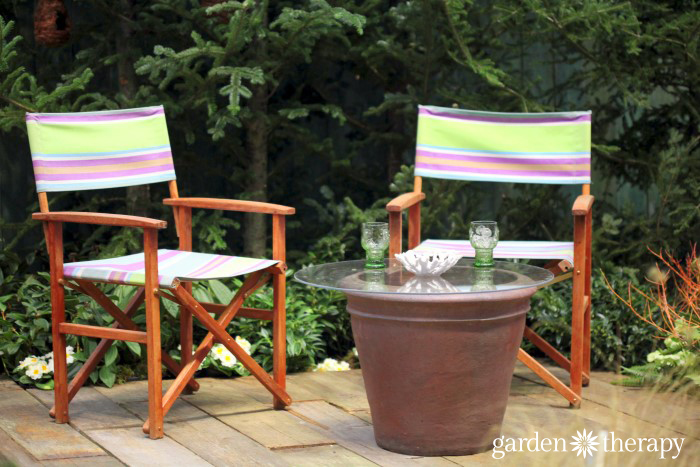 Outdoor table made from a large pot and a glass top from the Blue Greenhouse Seaside Garden Design Feature