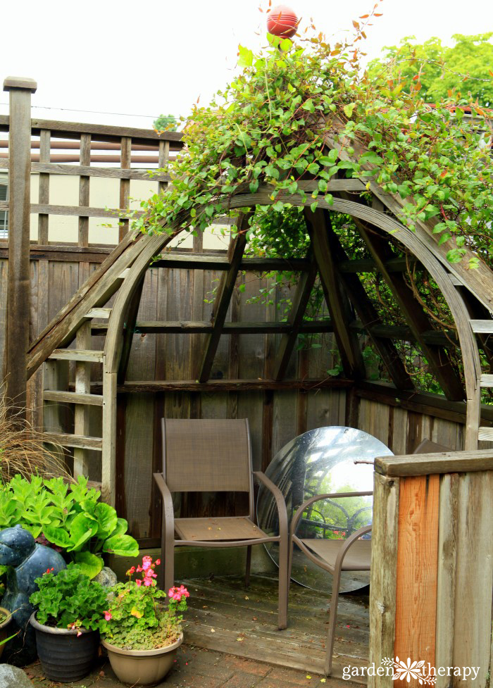 corner seating inside an arched trellis and a large circular mirror resting on the ground