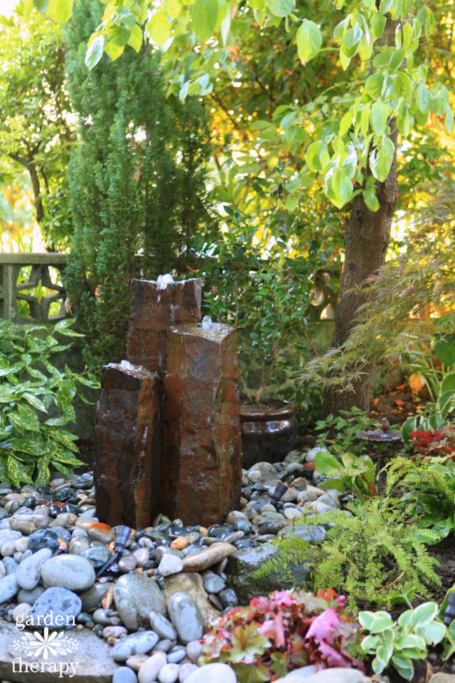 water bubbling out of a water fountain on top of river rocks in a garden