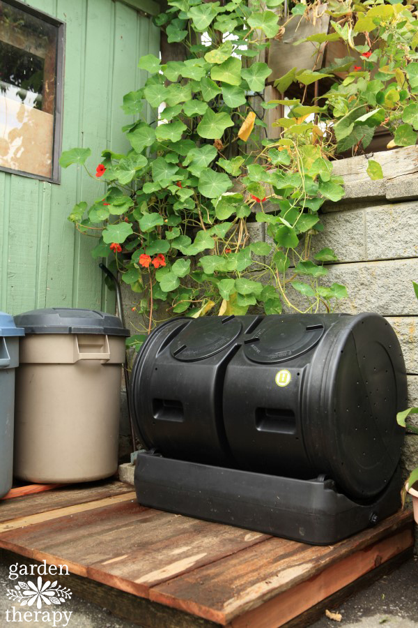 composting station after makeover with compost tumbler on raised wooden platform and garbage bins