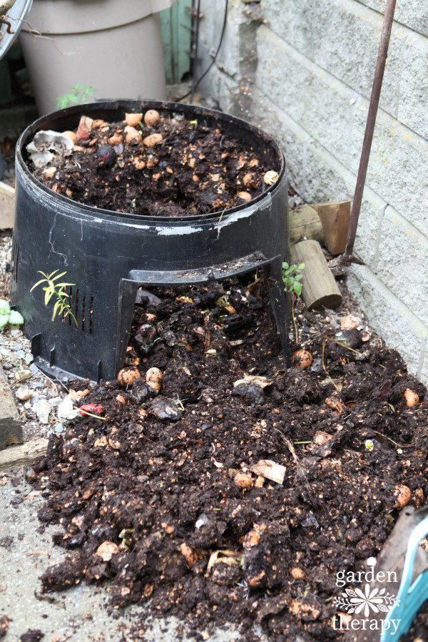 open top compost bin with compost spilling out the side of the container all over the grround