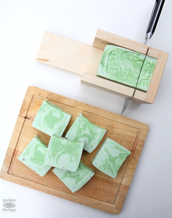 cutting a swirly green and white cedarwood soap mould onto a cutting board