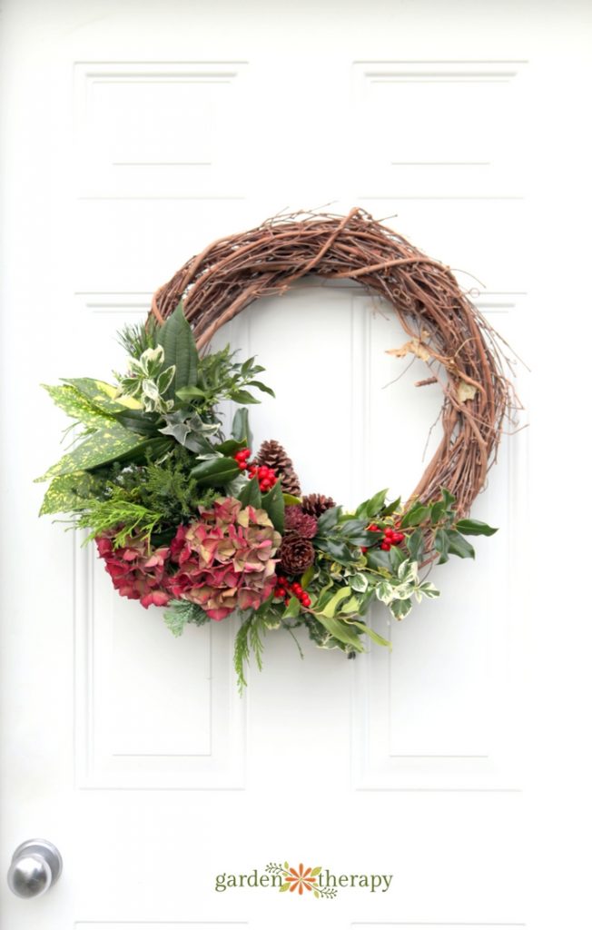 asymmetrical wreath with lots of fresh Christmas greenery including a dried pink hydrangea