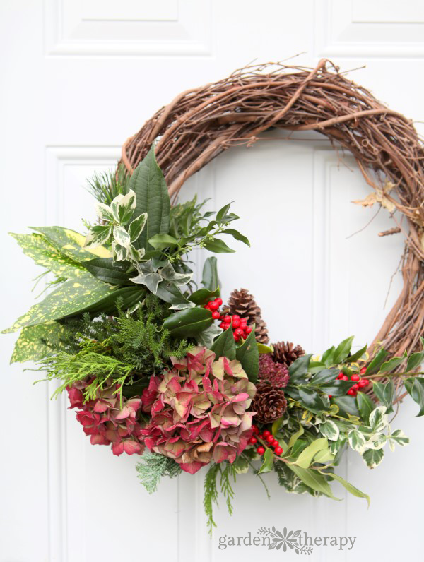 close up of an evergreen wreath with highlights of red with pinecones on a white door