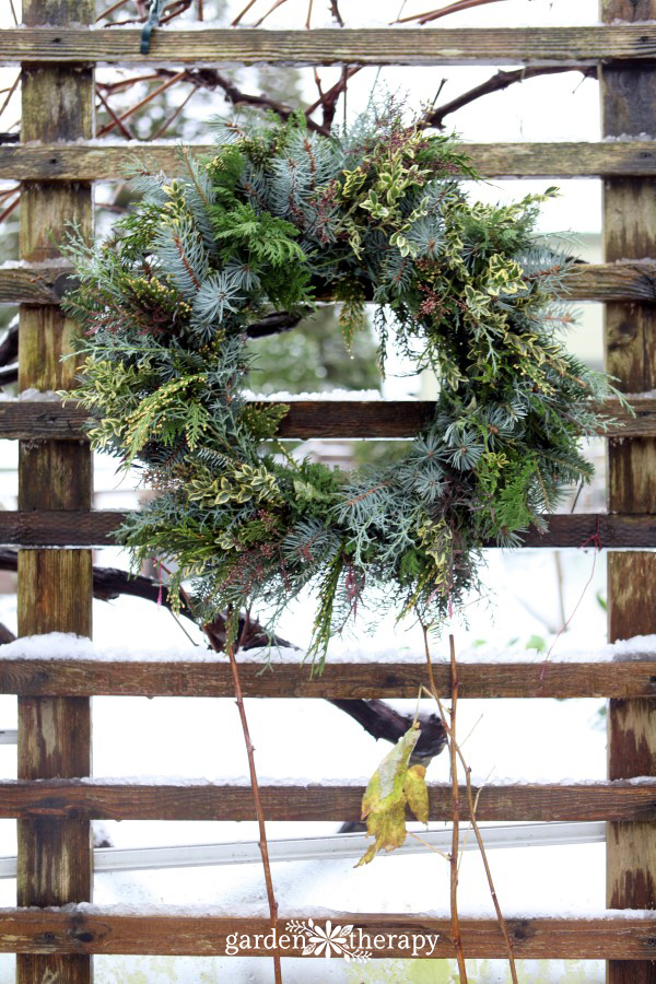 DIY Christmas wreath on wire frame hanging on a wooden fence with snow