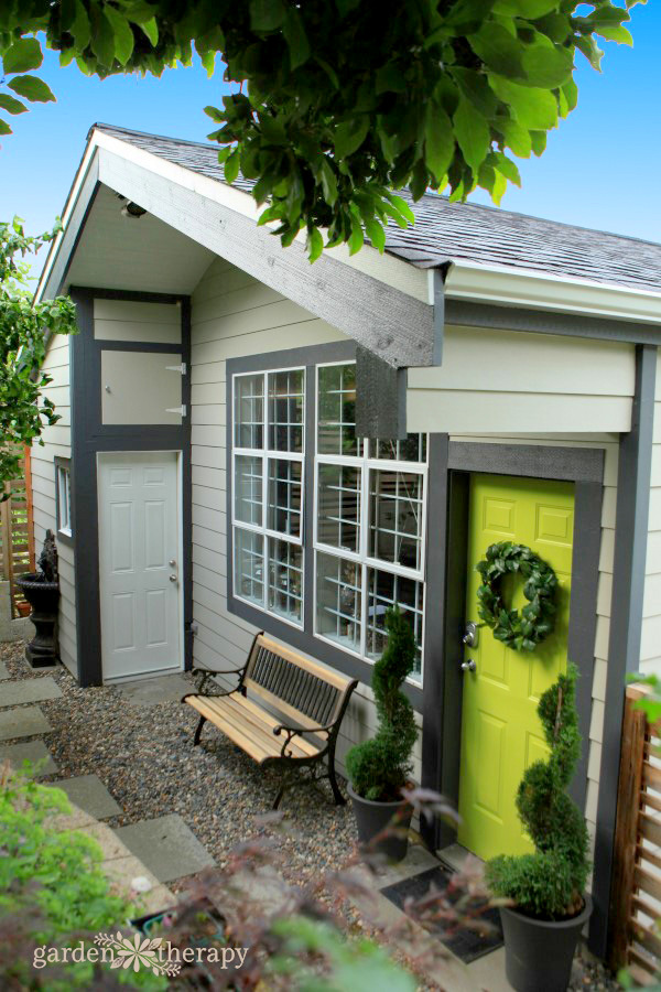 grey she-shed with a vibrant green door with a wreath