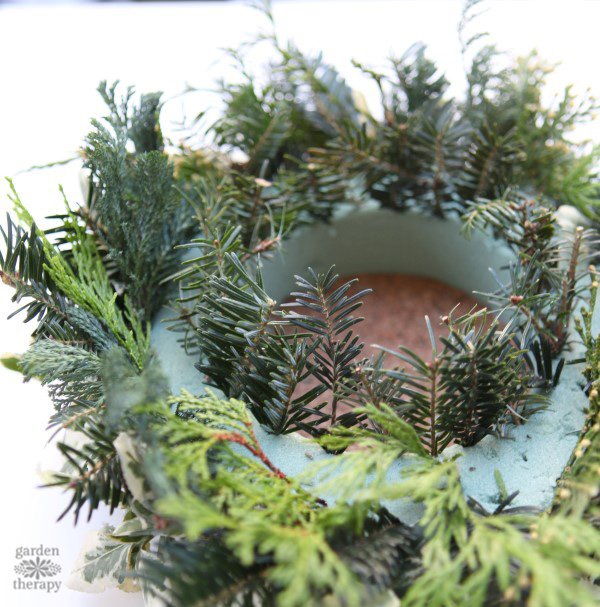 Un centro de mesa navideño de bricolaje festivo con mucha vegetación y piñas del patio trasero