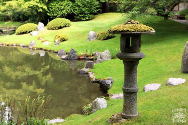 Japanese garden pond edge with carpet of green moss and a concrete lamp post