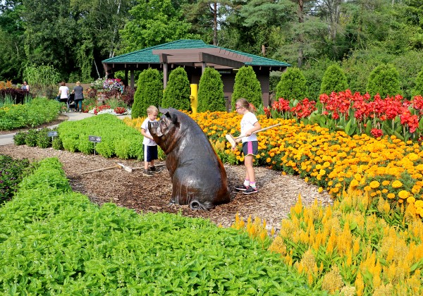 A large sculpture of a pig with two children standing beside it in the center of a garden