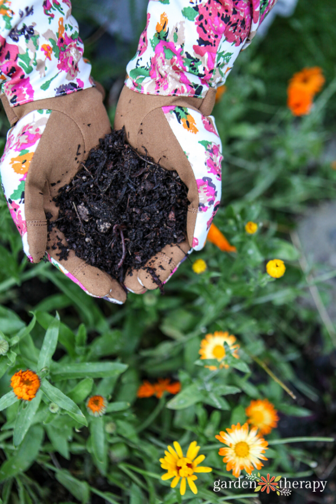 Woman holding custom garden soil in her cupped hands over flower bed.