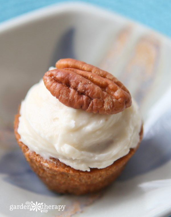 A mini carrot cake cupcake topped with cream cheese frosting and a pecan.