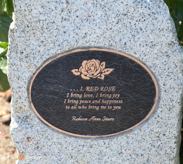 Plaque that reads " I, red rose, I bring love, I bring joy, I bring peace and happiness to all who bring me to you".