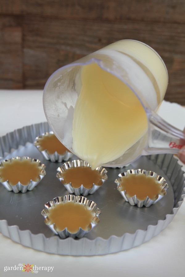 carefully pouring beeswax into tart molds to make floating candles