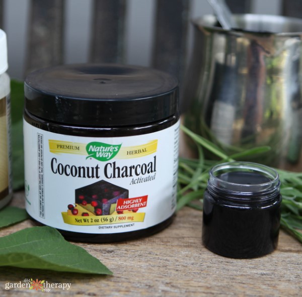 container of activated charcoal next to a small glass container of diy drawing salve