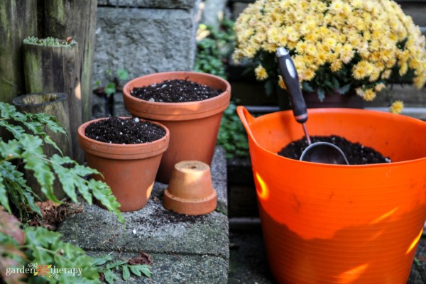Terracotta post filled with soil and an orange plastic bucket with soil and a trowel inside