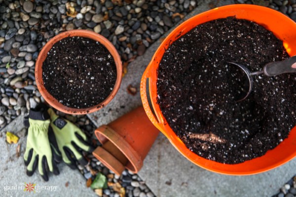 Two containers filled with soil with garden gloves and two small flowerpots