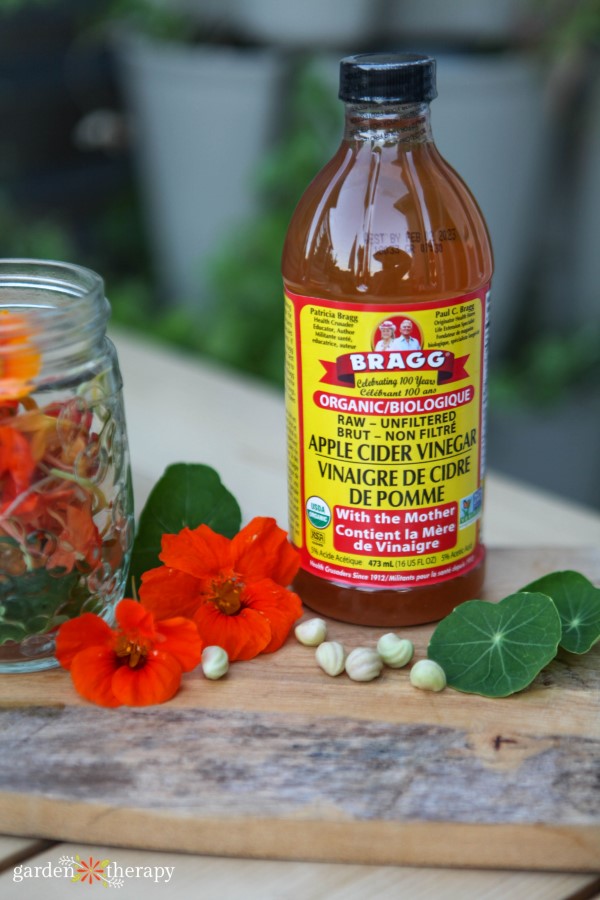 Apple cider vinegar with fresh nasturtium flowers and leaves on a wooden surface