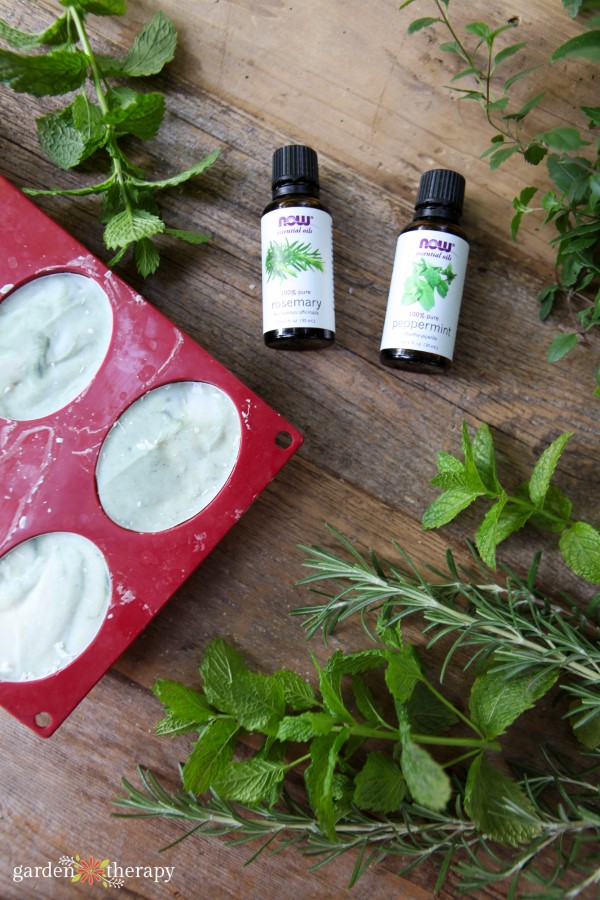 rosemary and spearmint essential oil next to the fresh herbs and soap in a mold