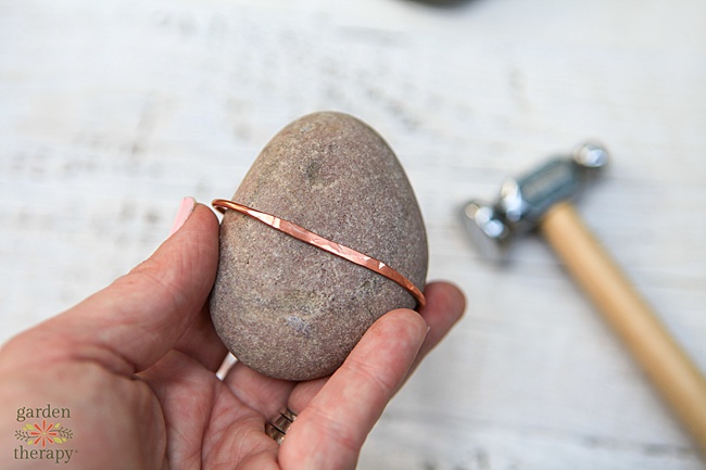 Copper wire flattened against a river rock with a hammer in the background.