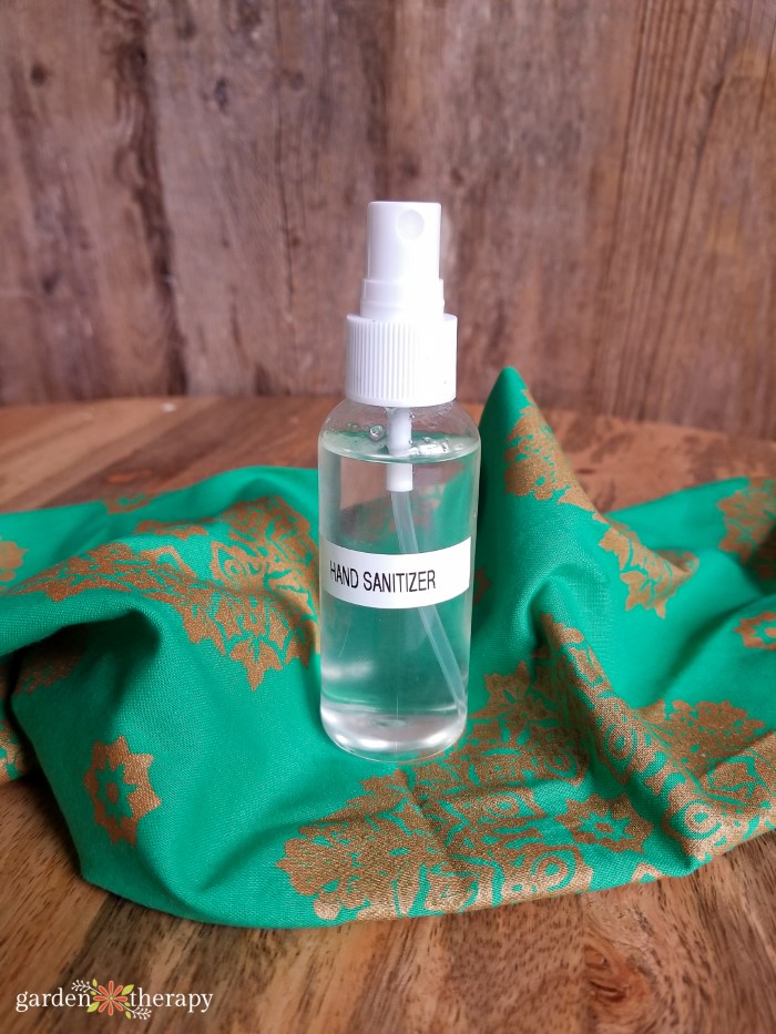 Homemade bottle of spray sanitizer on a green and gold napkin on top of a wood table.