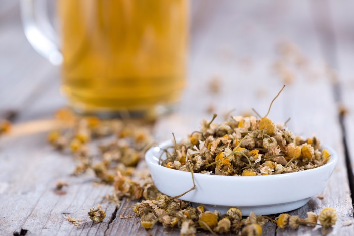 Dried chamomile flowers with chamomile tea in the background.