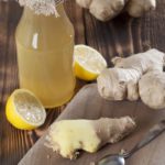 Peeled ginger root with lemons and a bottle of ginger syrup in background.