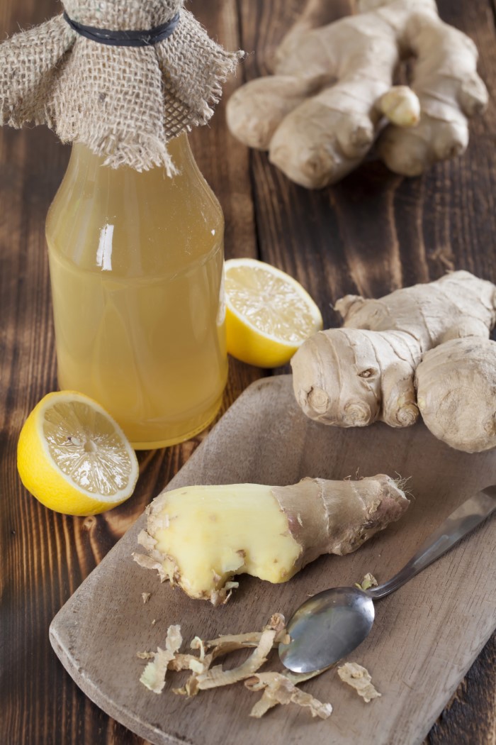 Peeled ginger root with lemons and a bottle of ginger syrup in background.