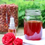 rose water in a mason jar and spray bottle with roses and dried rose petals on the table