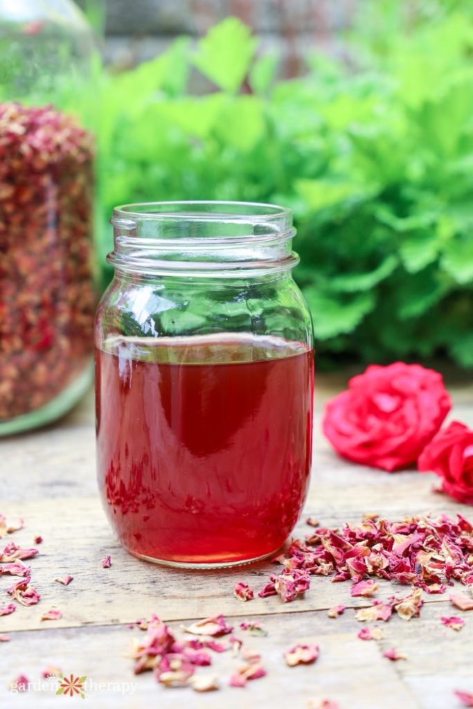 rose water in a mason jar with dried rose petals in another jar and on the table