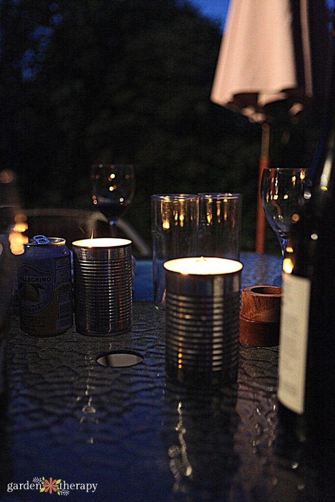 candles in cans lit at night on a table with bottle of wine and glasses