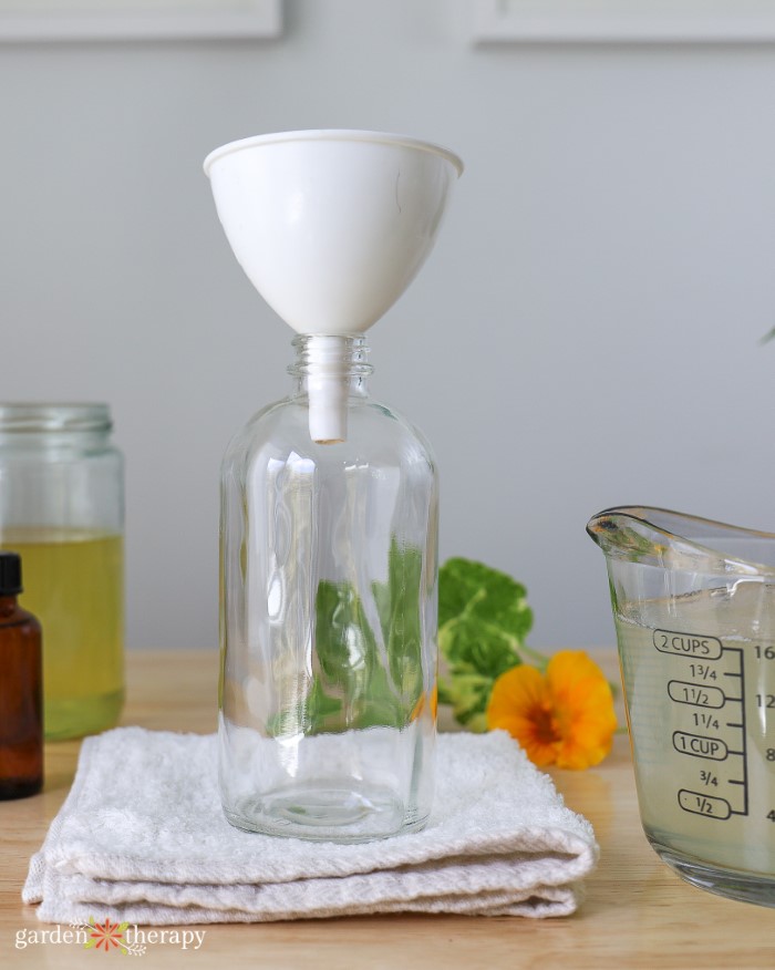 Pouring aloe vera soap into a glass soap bottle with a funnel. 