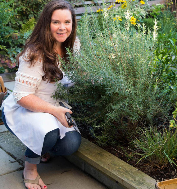 Stephanie Rose kneeling in front of a rosemary bush