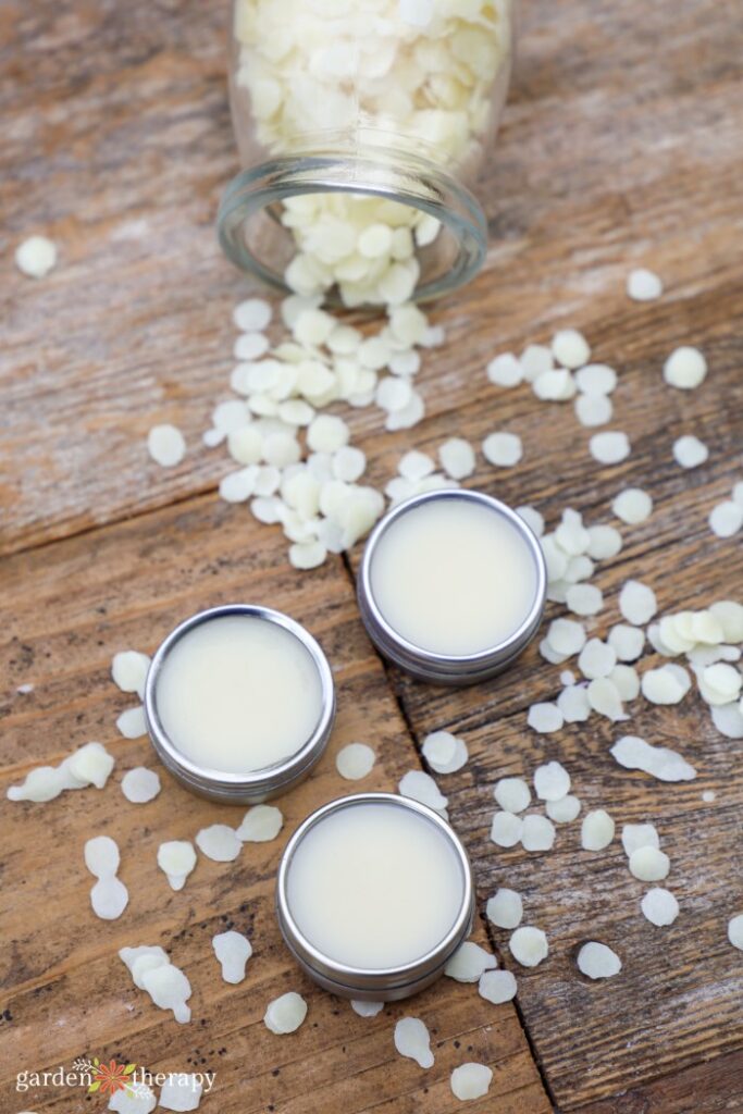 mint lip balm in small metal tins surrounded by spilled beeswax on a wood surface