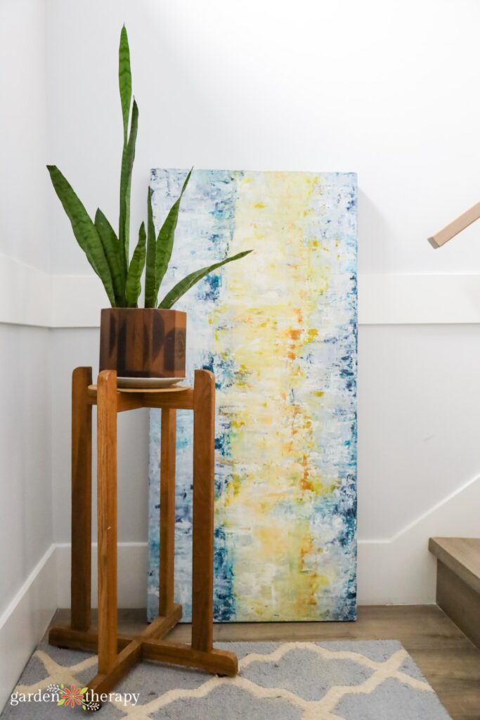 snake plant in a wood plant stand and artwork resting on the floor next to it