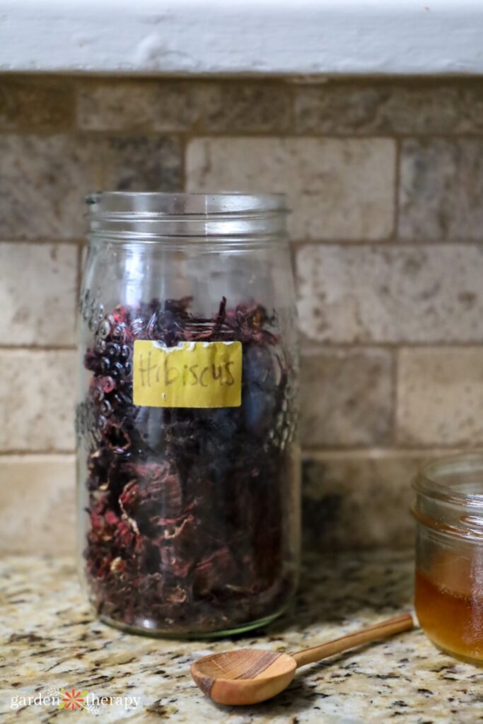 dried hibiscus flowers in a jar with a wooden spoon