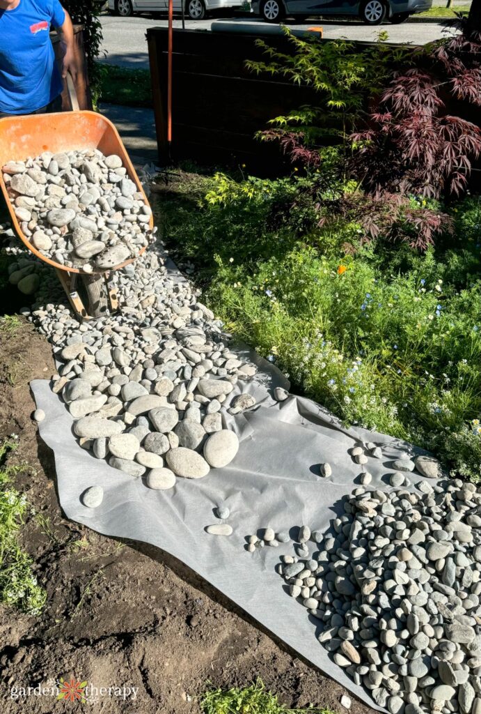 pouring river rocks onto landscape fabric for a dry river bed