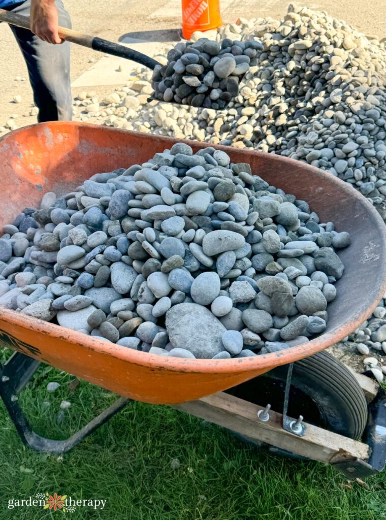 river rock in wheelbarrow for dry river bed being scooped with shovel