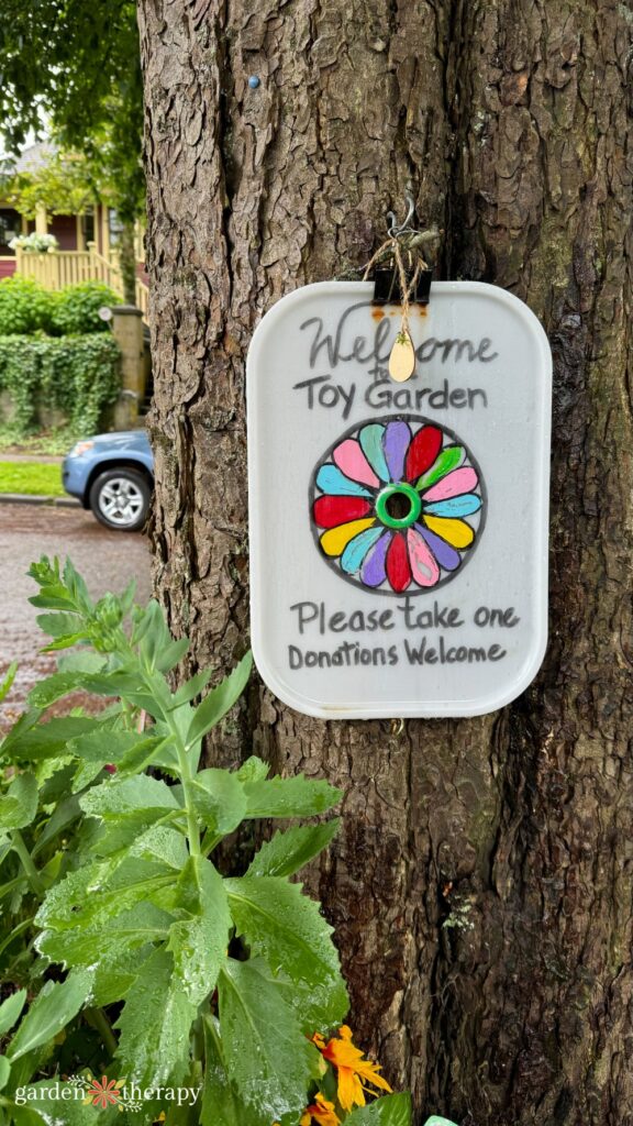 sign attached to street tree reading, "Welcome to the toy garden. Please take one. Donations welcome."