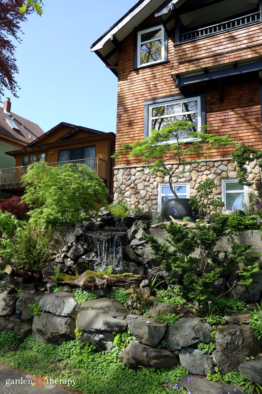 Japanese inspired front yard garden and fountain in front of wood and stone siding house