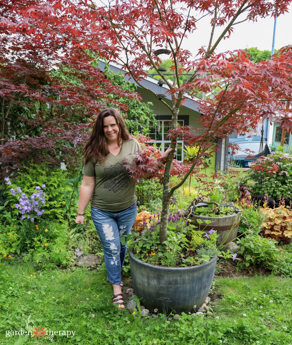 Stephanie smiling in garden with potted Japanese maple